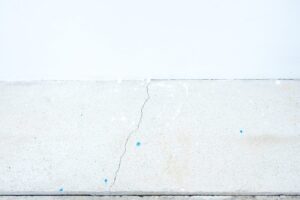 Fissure sur une dalle béton au pied d'un mur de maison