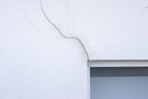 Fissure partant de l'angle d'une fenêtre sur une façade enduite